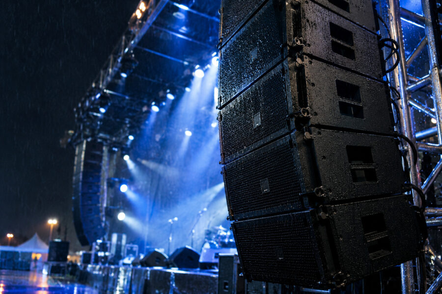 Polyurea-coated speaker cabinets at an outdoor concert in rain, showing waterproof protection for pro audio touring equipment